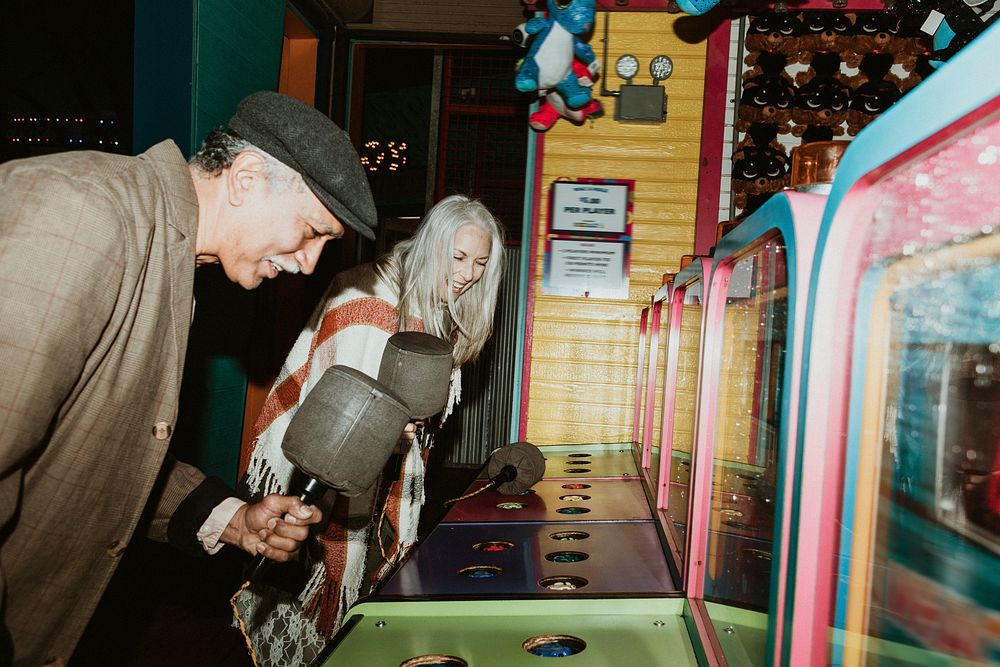 Happy senior couple playing whack a mole at a game arcade