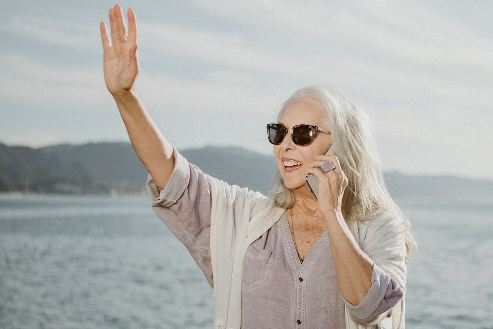 Senior woman on the phone waving by the sea