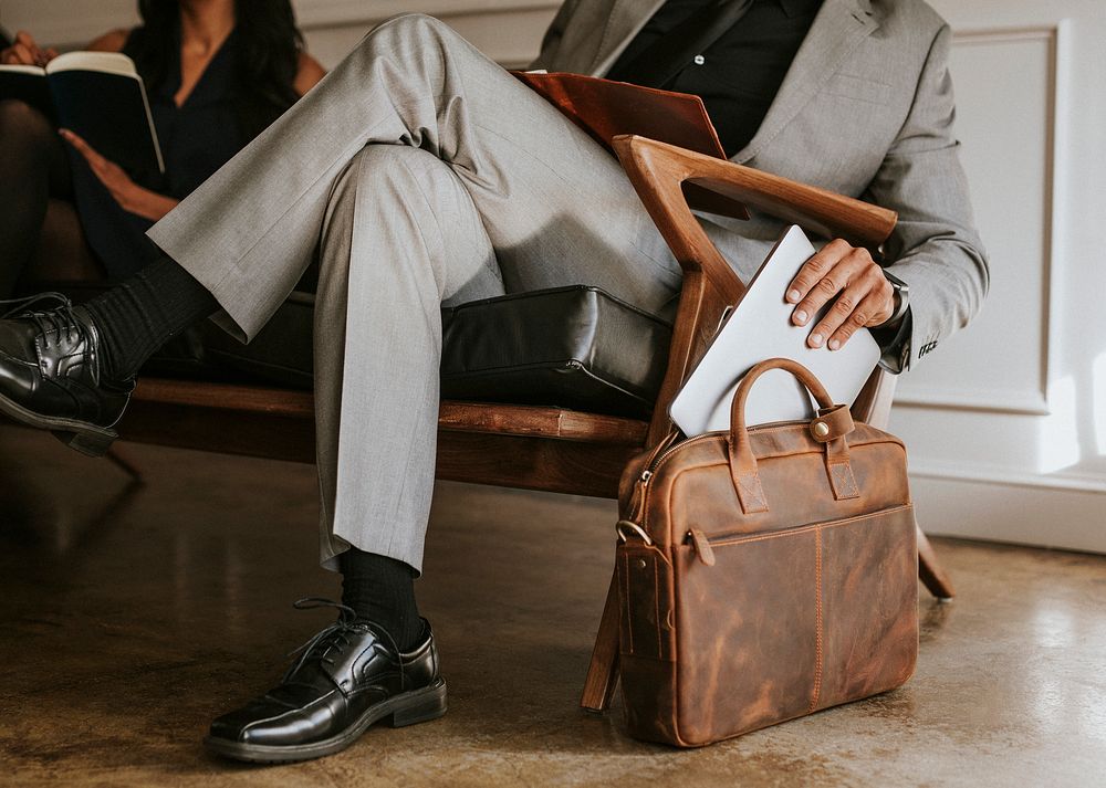 Classy businessman putting his laptop in his brown leather bag