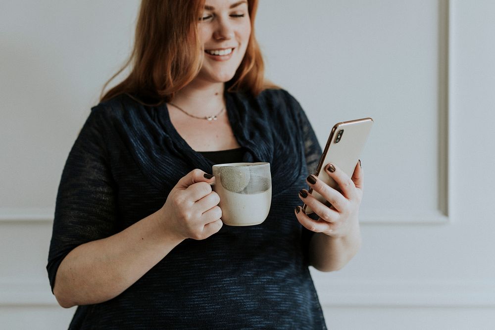 Happy woman having her coffee and playing on the phone