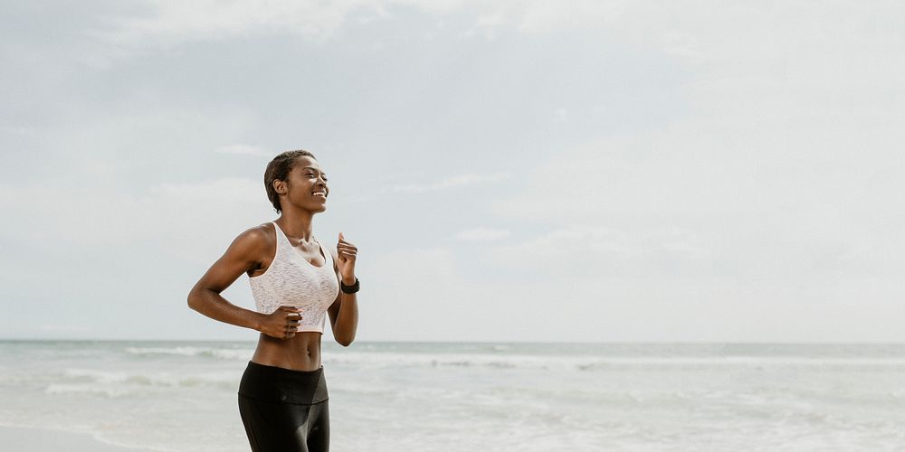 Happy black woman jogging on the beach