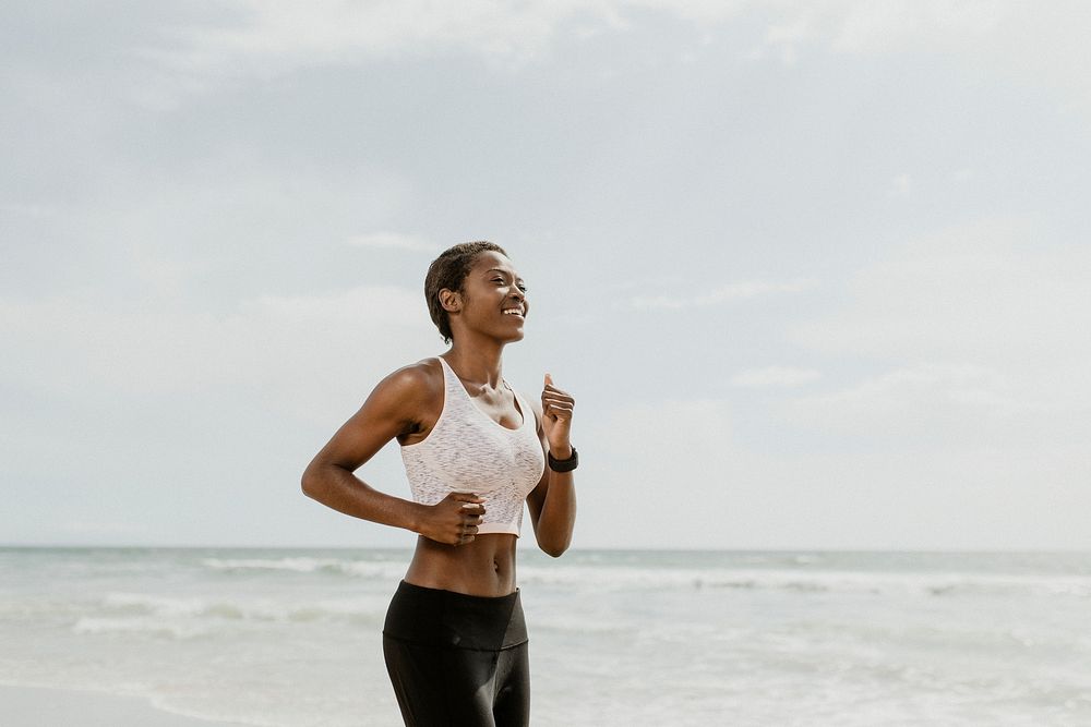 Happy black woman jogging on the beach