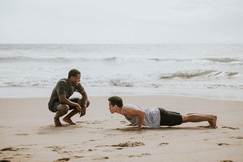 Man doing pushups with a trainer at the beach