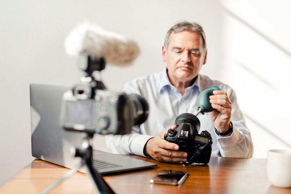 Man cleaning his camera lens with a rubber air blower