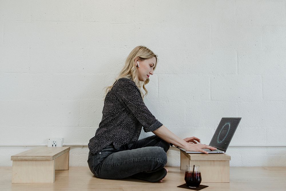 Cheerful blond woman using a laptop on a wooden floor