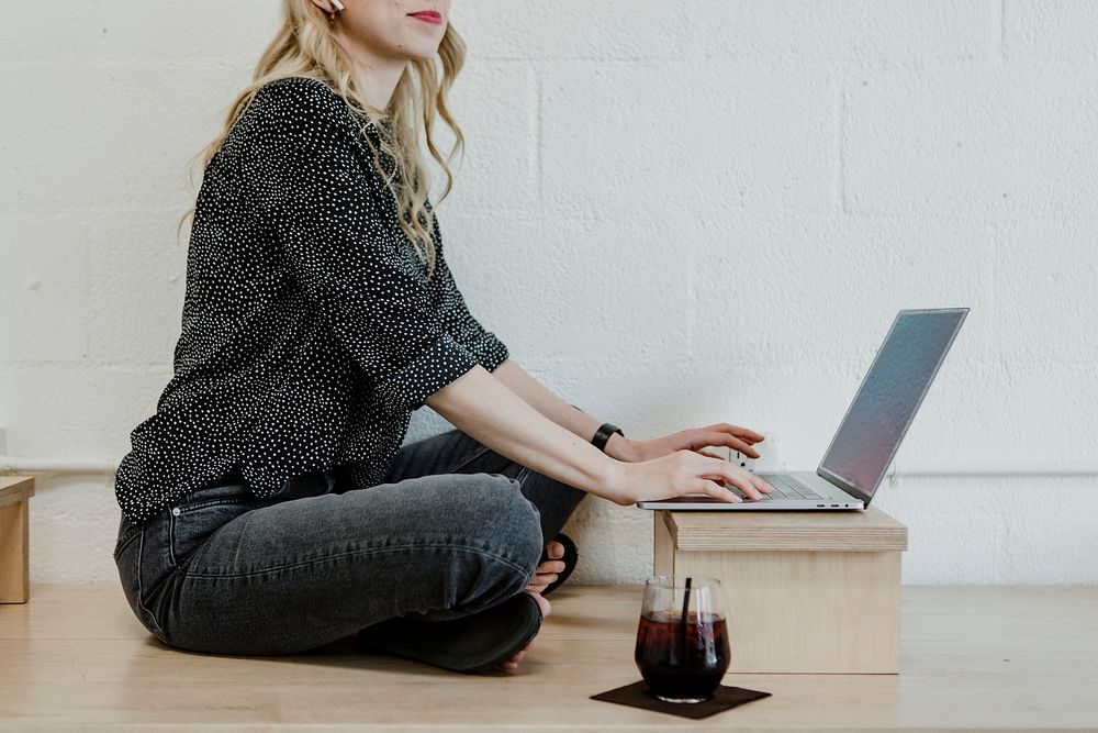Cheerful blond woman using a laptop on a wooden floor