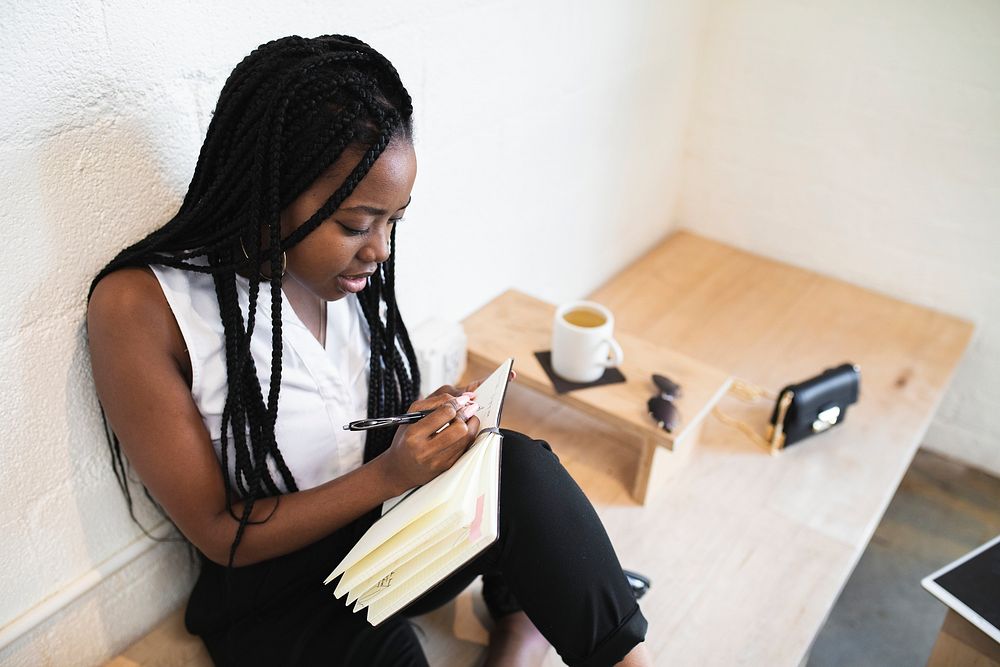 Black woman writing on a notebook in a cafe