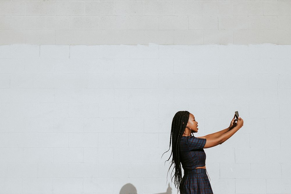 Black woman taking a selfie at a white wall