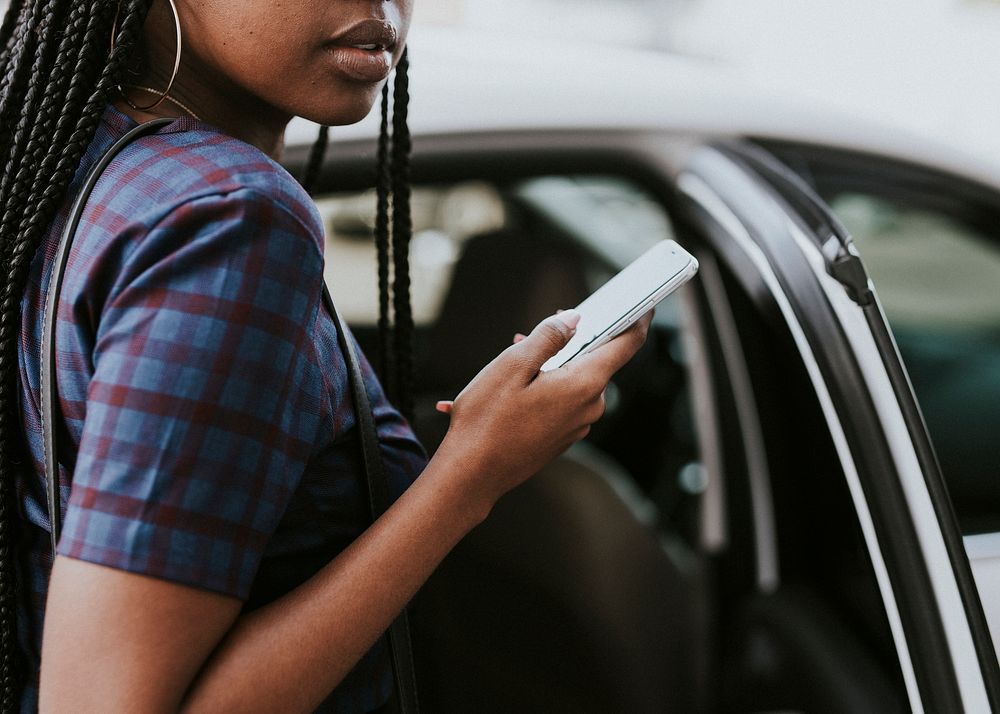 Black woman holding her phone while getting into a car