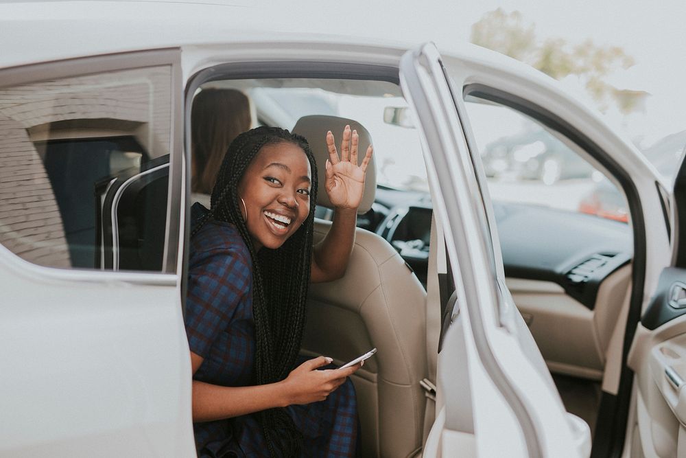 Happy black woman waving goodbye from a car