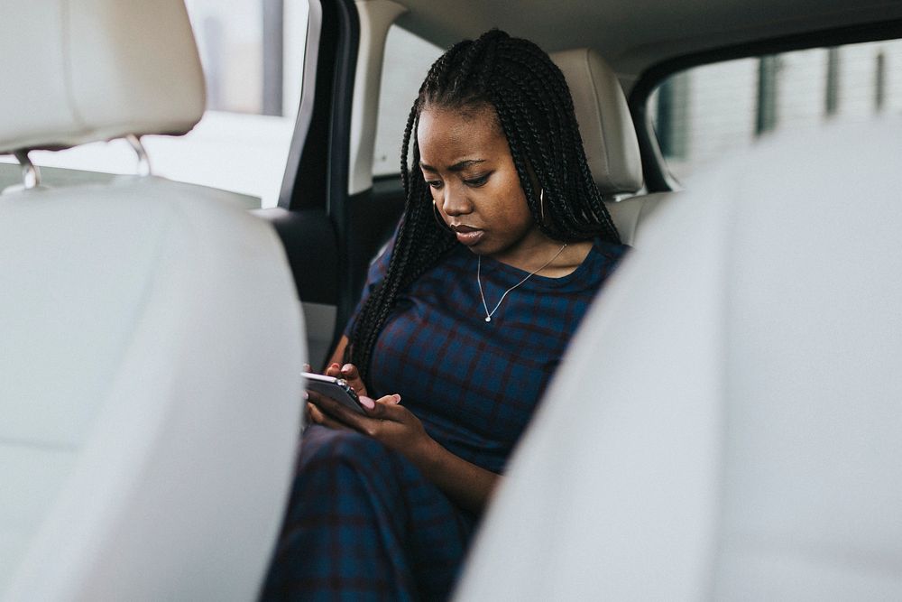 Black woman sitting in the passenger seat using her phone