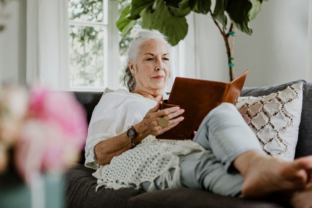 Elderly woman reading a book on a sofa in a weekend