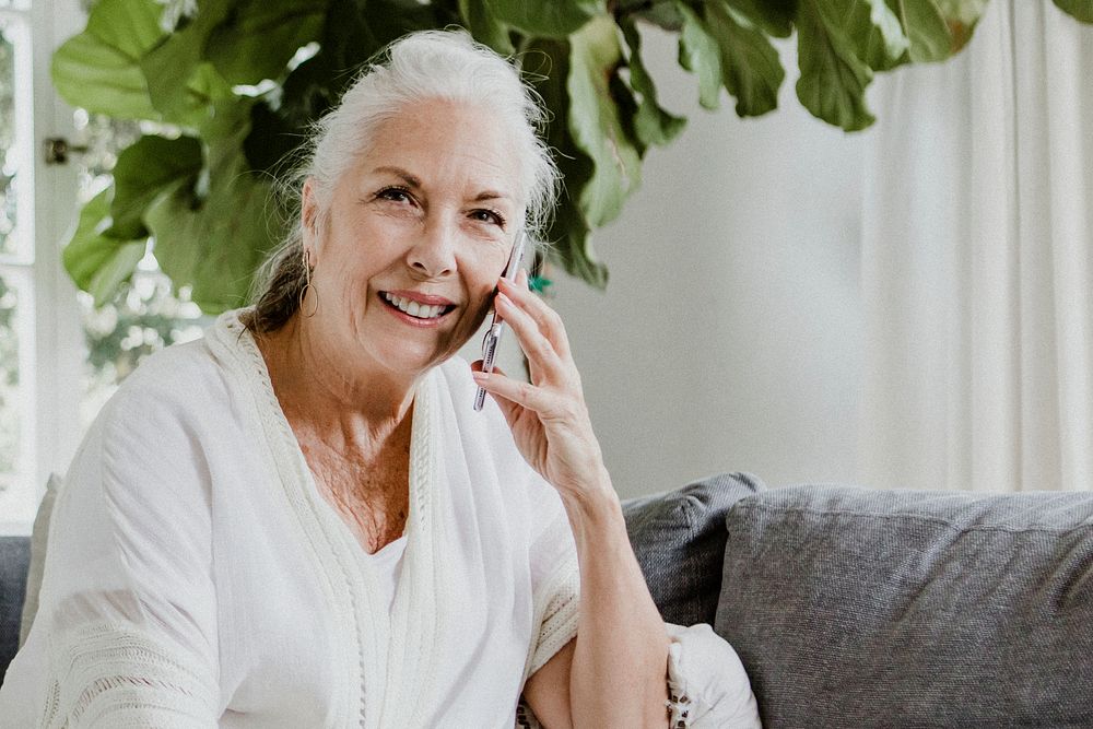 Cheerful elderly woman talking on a phone on a couch
