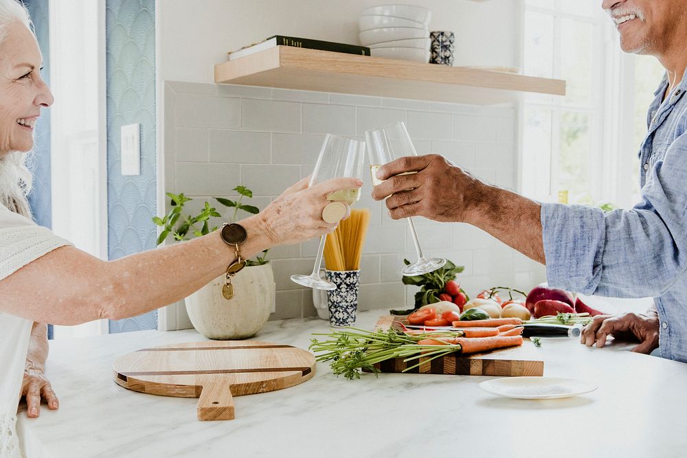 Cheerful elderly clinking their white wine in a kitchen