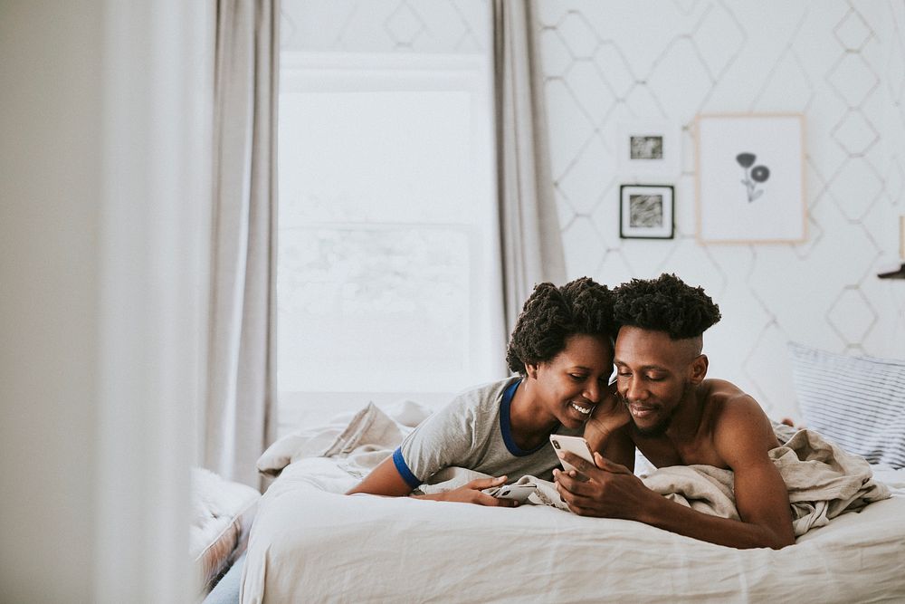 Happy black couple playing on a smartphone in bed
