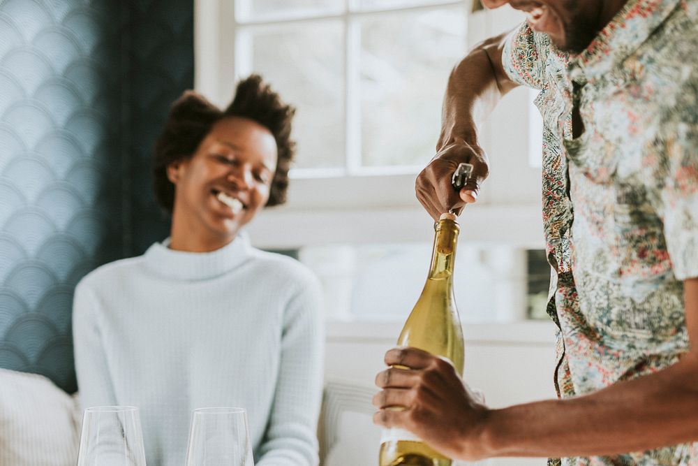 Happy black man uncorking a wine bottle