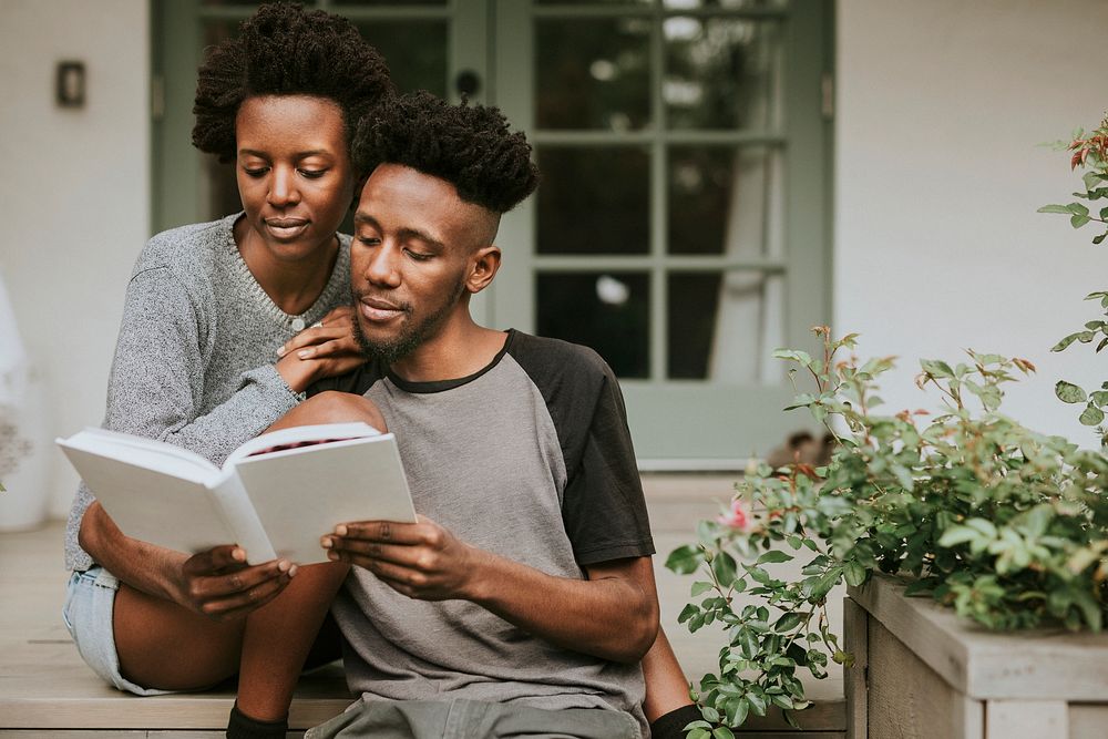 Cute black couple reading a book together in a garden