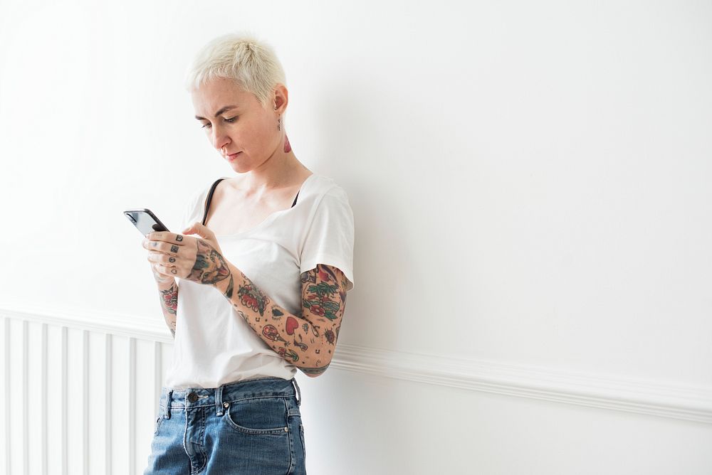 Tattooed woman using her phone by the white wall