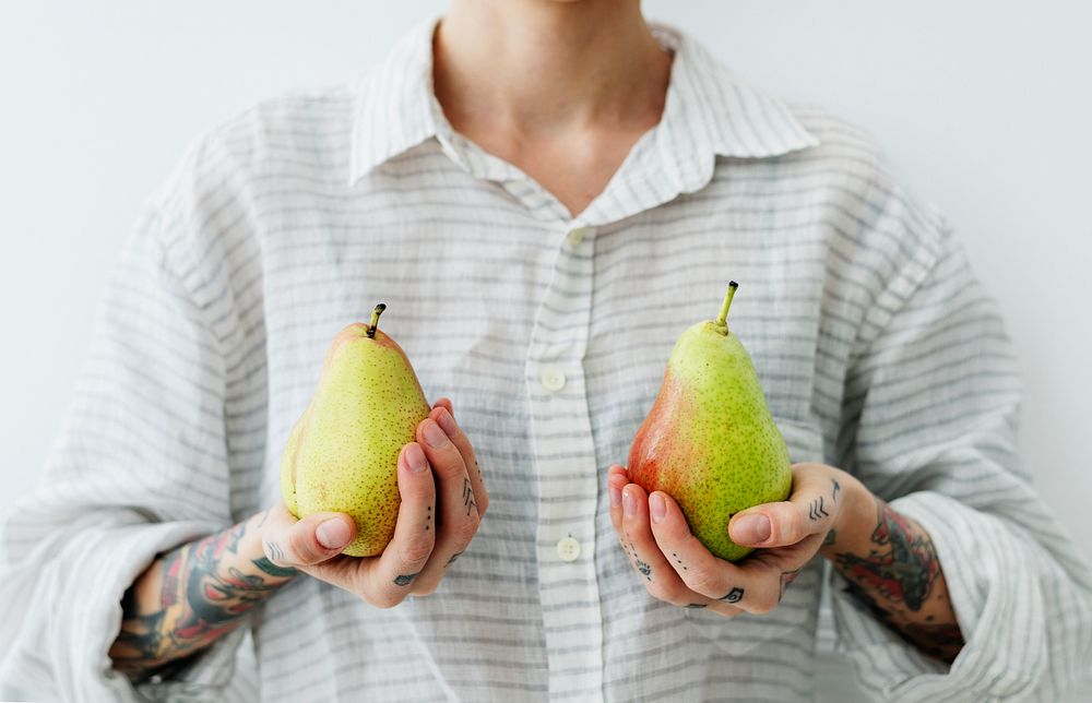 Tattooed woman in a linen shirt holding pears