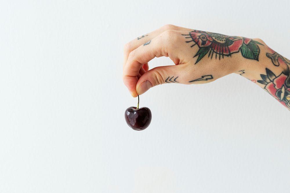 Tattooed hand holding a fresh cherry