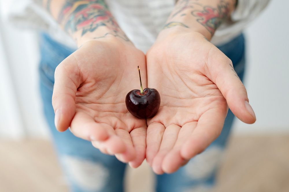 Tattooed woman showing a cherry in her hand