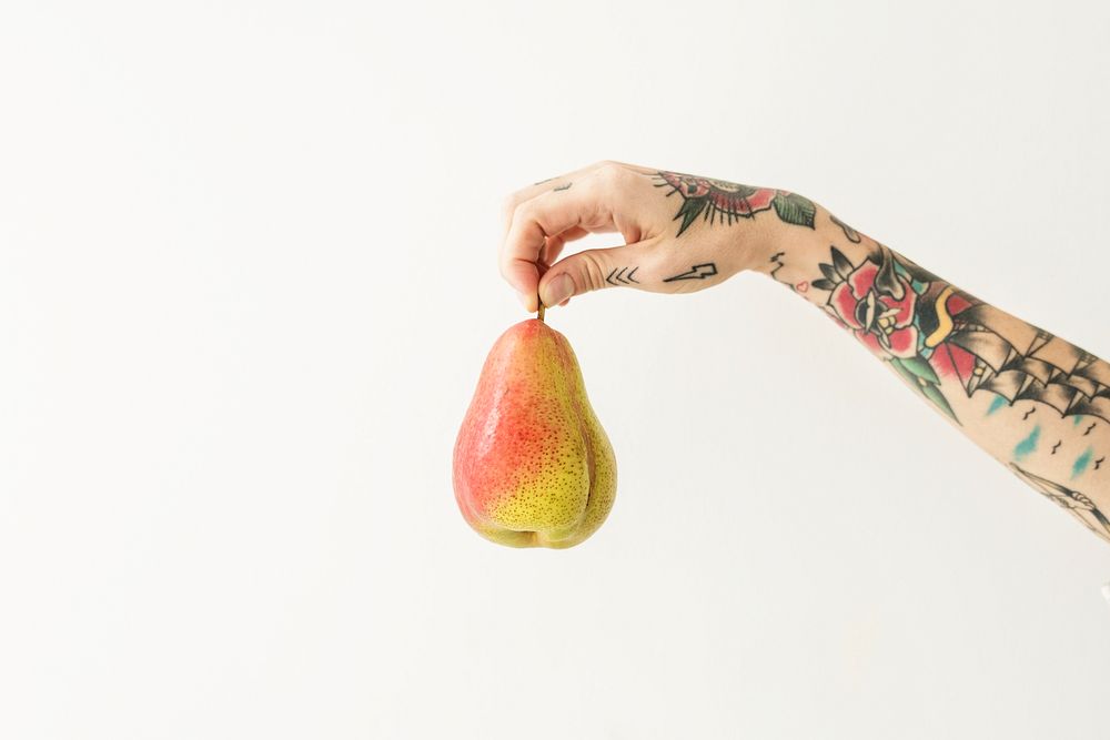 Tattooed hand holding a fresh red blush pear