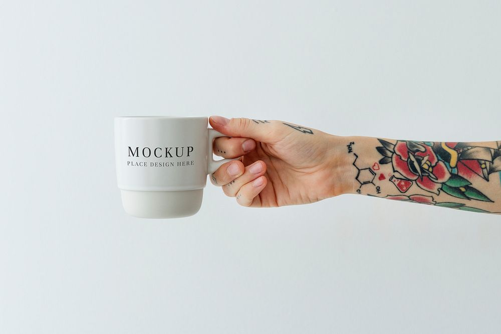 Tattooed hand holding a white coffee cup mockup