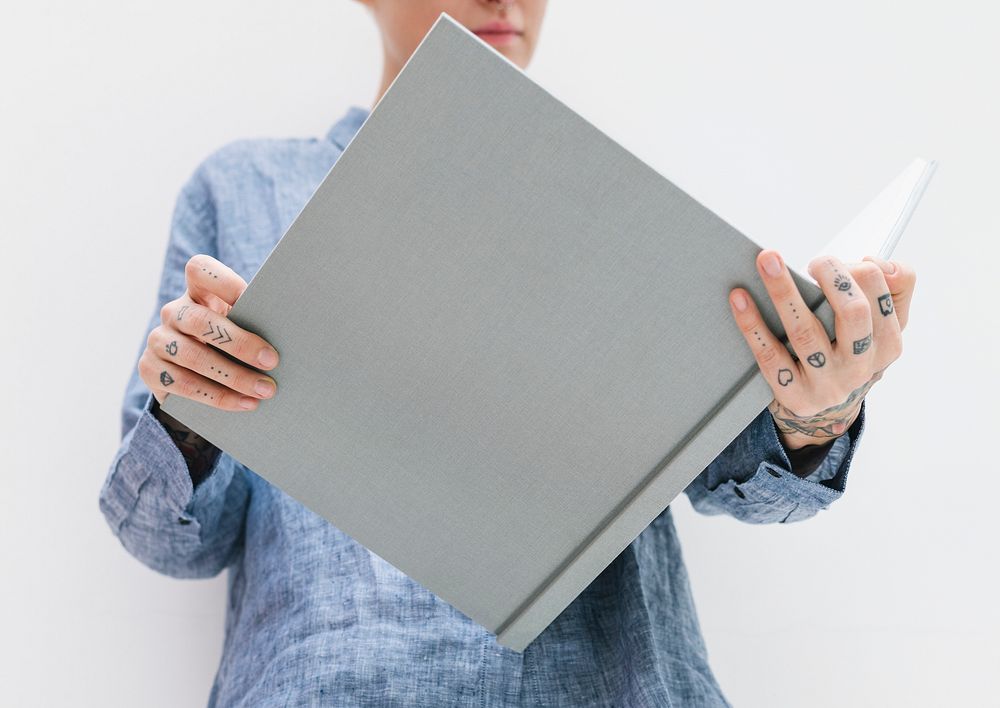 Tattooed woman in a blue linen shirt holding a book mockup
