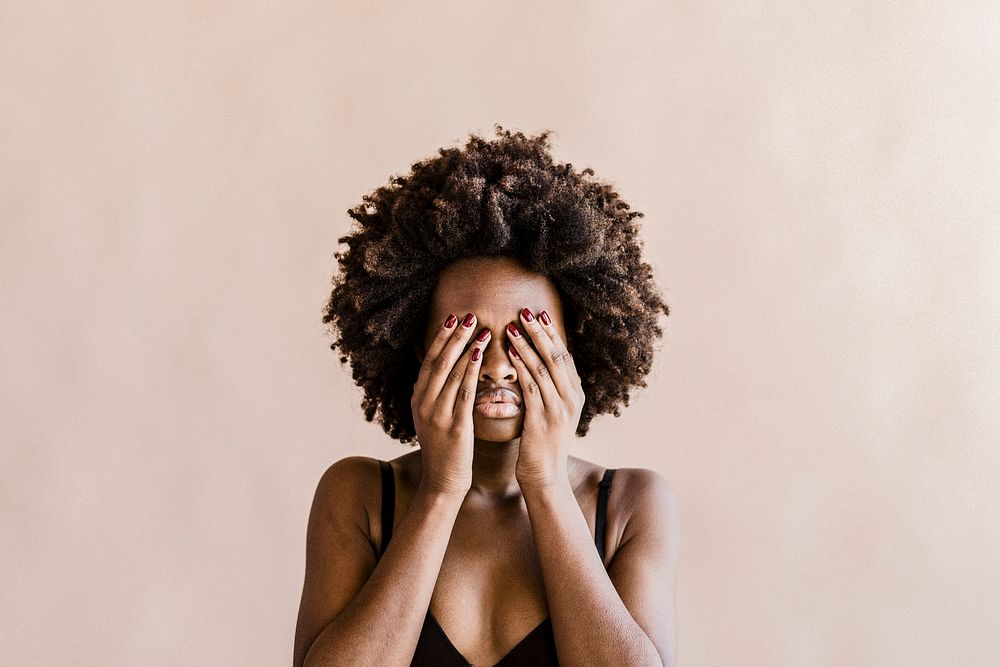Black woman with afro hair covering her face with hands