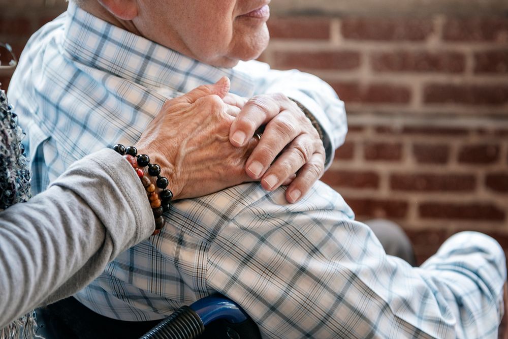 Elderly man on a wheelchair holding his wife hand on his shoulder