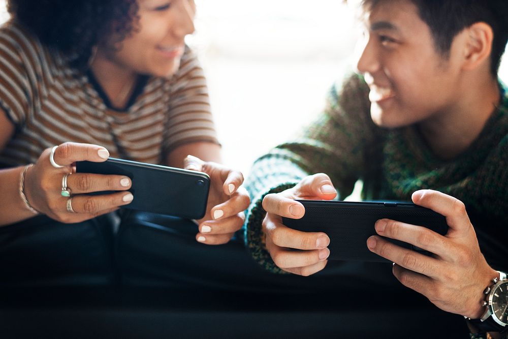 Cheerful couple playing online game on their phones