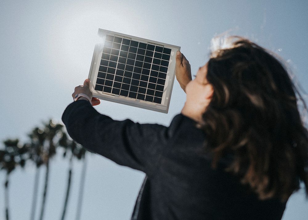 Rearview of eco-friendly woman holding a solar panel up in the sky