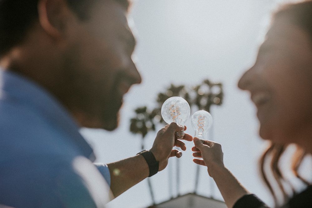 Eco-friendly couple holding the light bulbs up in the sky