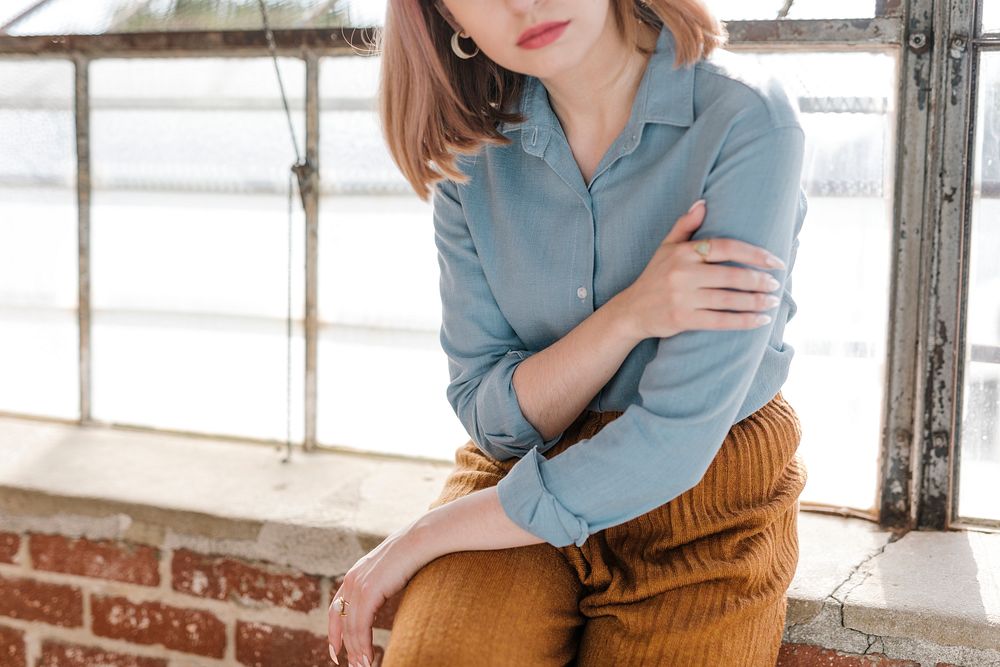 Cool woman in a blue shirt sitting on a brick wall