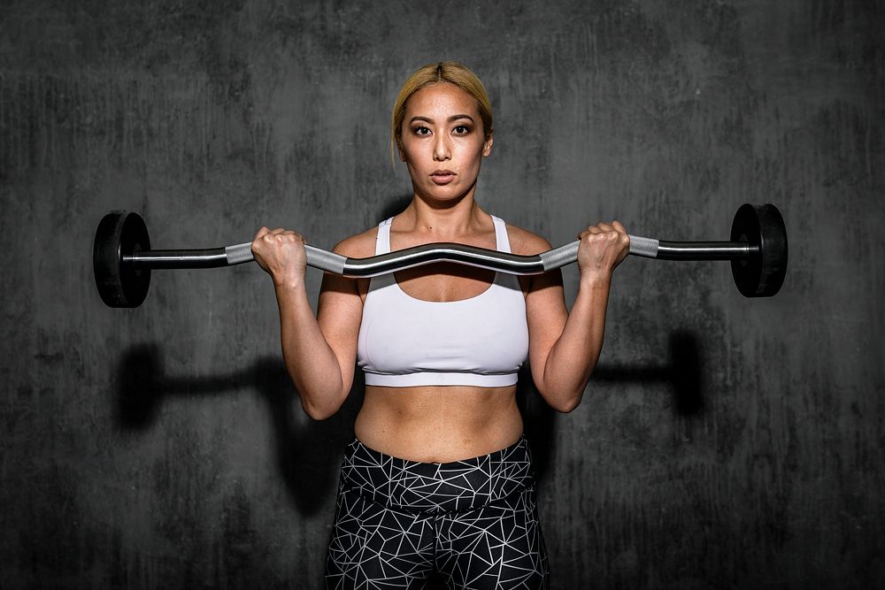 Woman exercising weighlifting with barbell at fitness gym