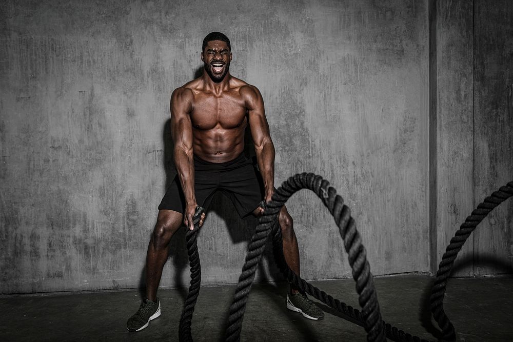 Muscular man working out on the battle ropes in a gym