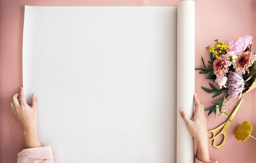 Woman unroll a paper on a pink table by a bouquet of flowers