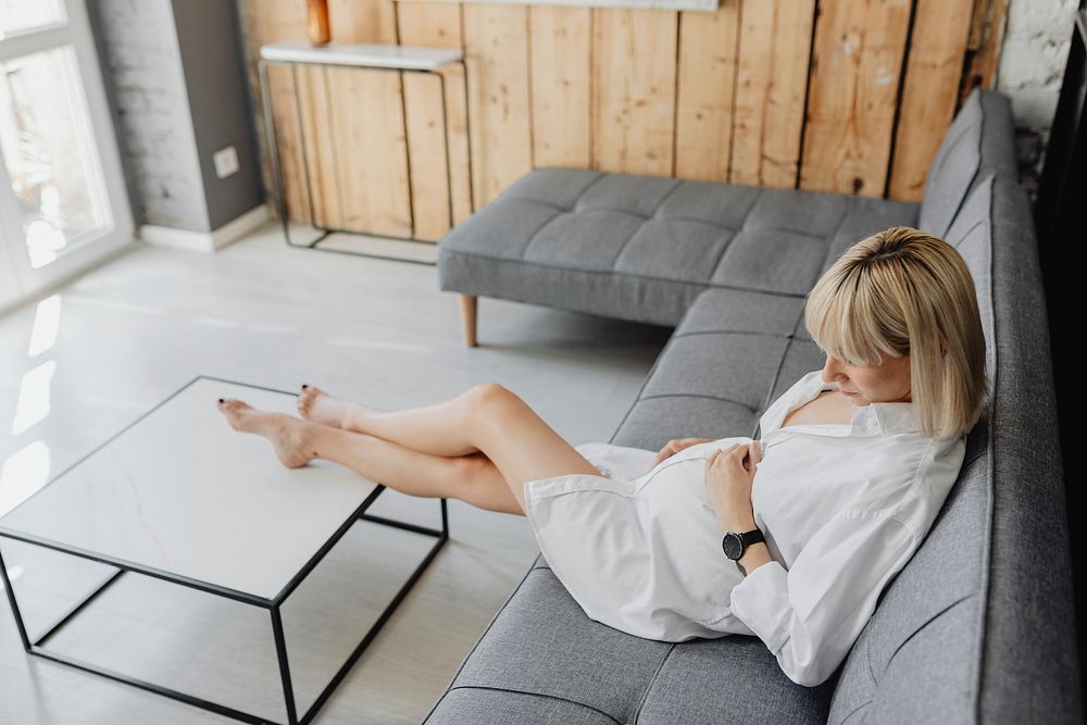 Pregnant blond-haired woman relaxing on a gray sofa