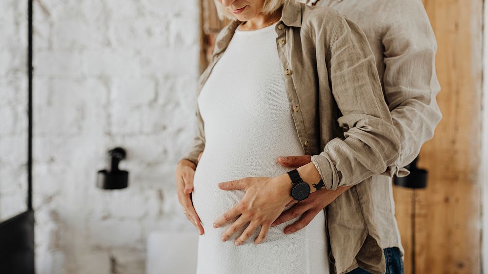 Husband holding his pregnant wife&rsquo;s baby bump blank space 