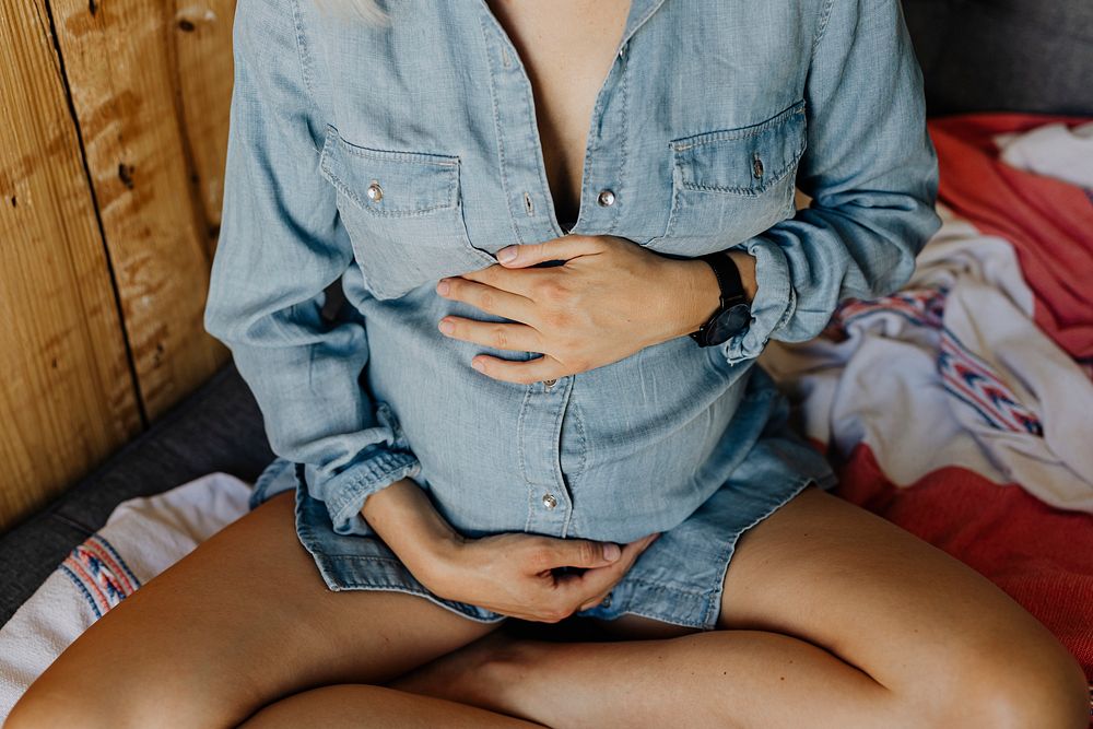 Pregnant woman in a denim shirt sitting on a sofa