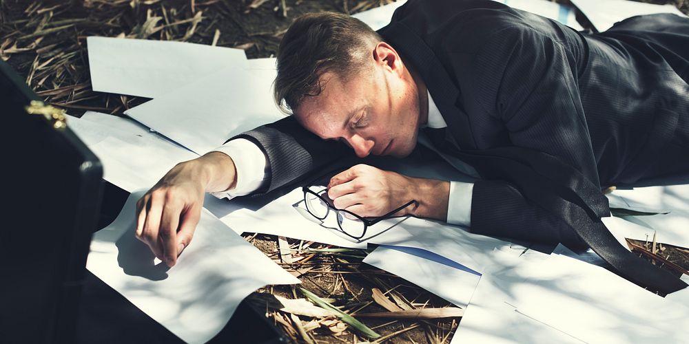 Exhausted business man passed out on the grass with paperwork
