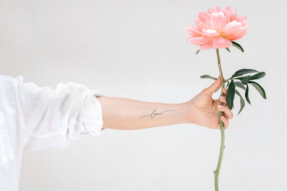 Woman with an arm tattoo holding a Peony The Fawn