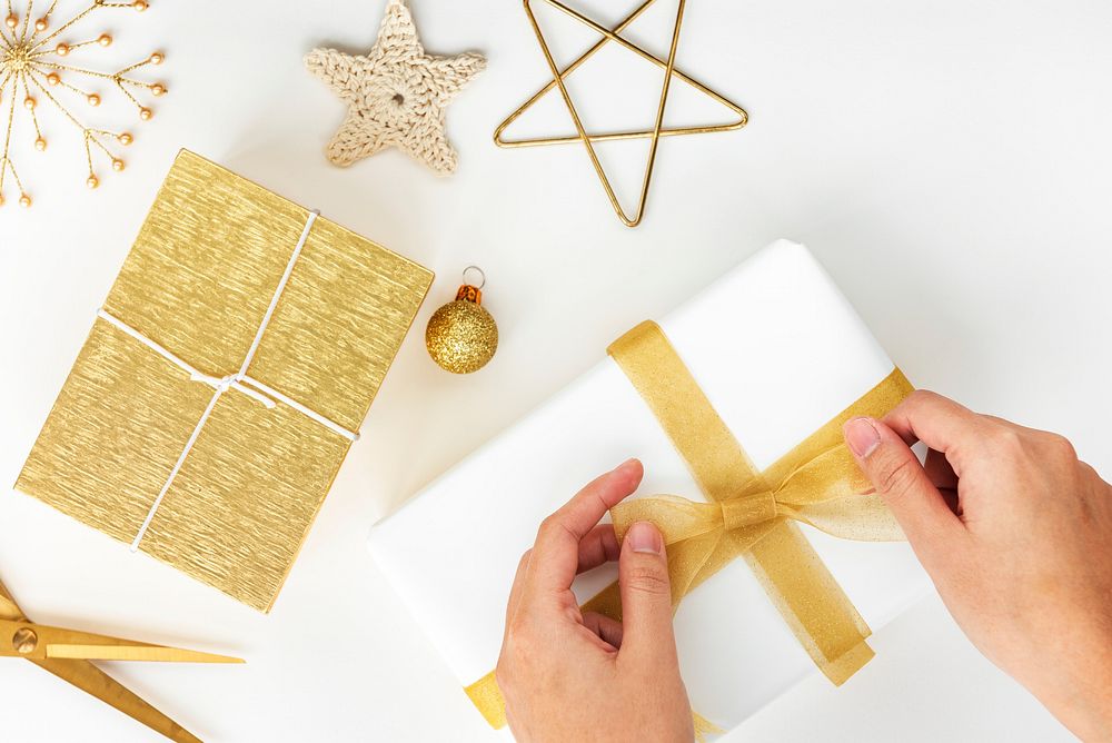 Woman tying a gold ribbon to a white present