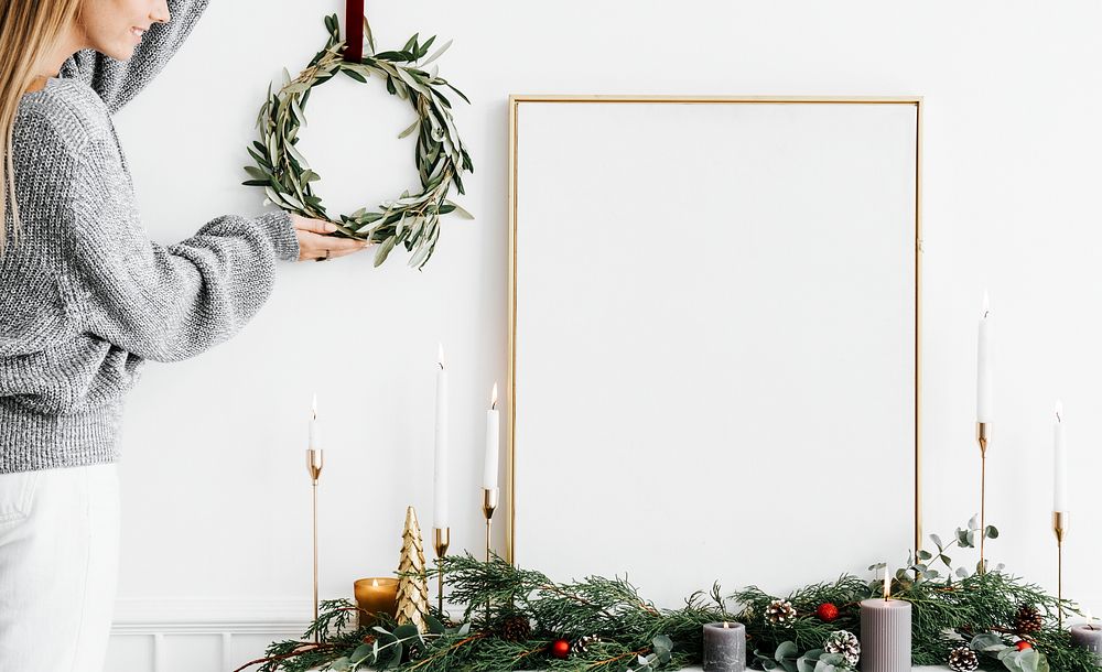 Woman hanging a Christmas wreath next to a blank white frame
