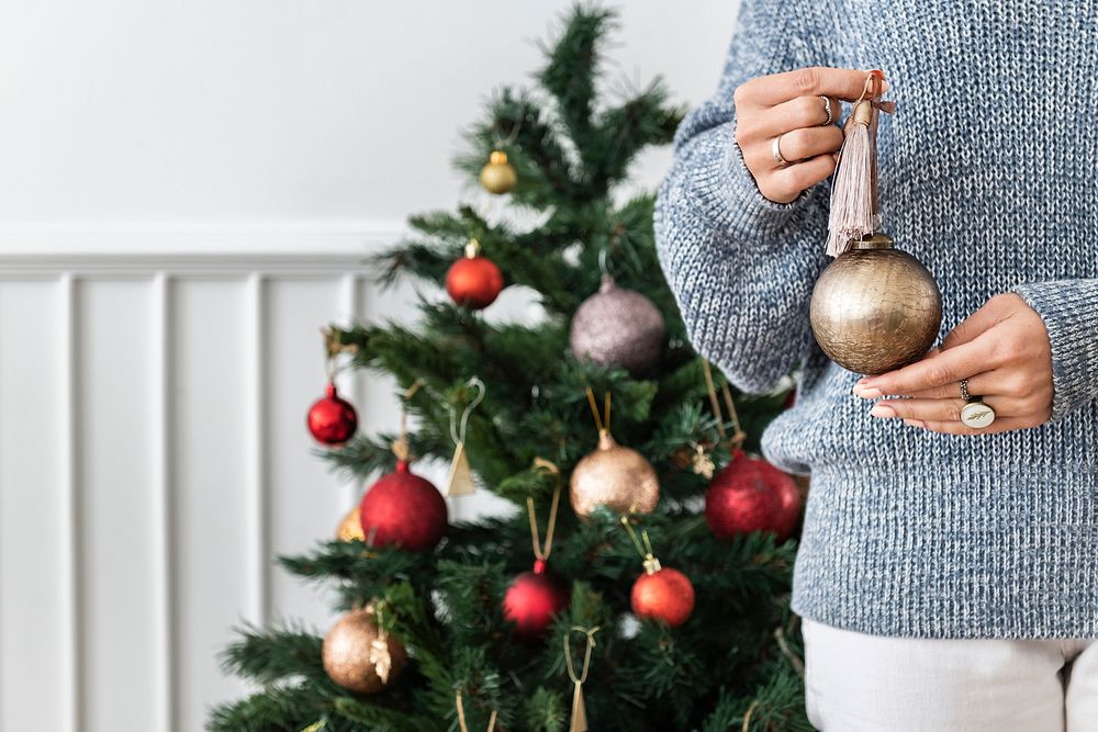 Woman holding a gold bauble in front of a Christmas tree