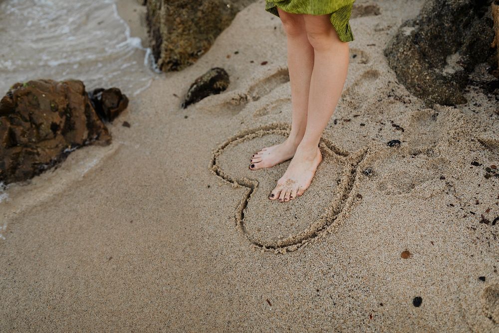 Woman standing in side a drawing heart on the beach