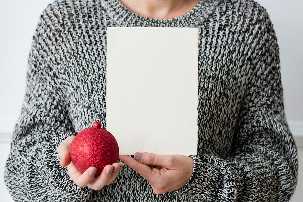 Woman holding a red bauble next to a white card mockup