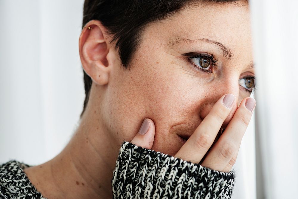 Woman in a gray sweater cover her mouth with fingers