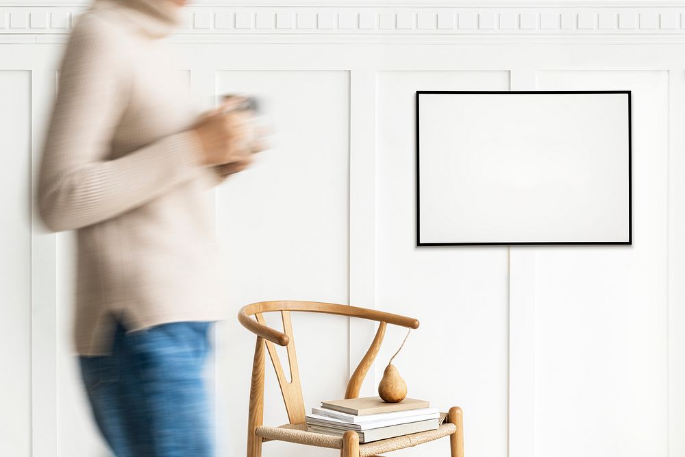 Woman walking past a black photo frame on a white wall mockup