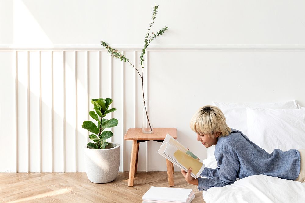 Blond haired Asian woman reading a book on a mattress on the floor